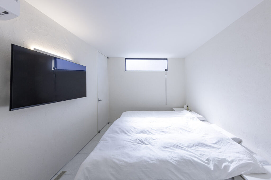 ベッドと壁掛けテレビだけで構成した、必要なものを厳選した寝室。奥にはトイレとシャワー室をまとめ、LDKなどの共有空間とプライベートスペースを明確に分けました。生活シーンに合わせて空間をゾーニングした、メリハリのある間取りです。
